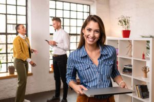 Beautiful young businesswoman standing in the office with her colleagues standing in the background.