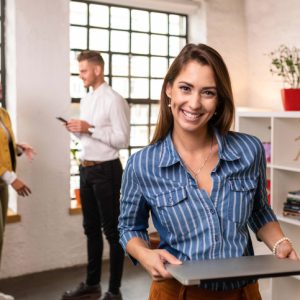 Beautiful young businesswoman standing in the office with her colleagues standing in the background.